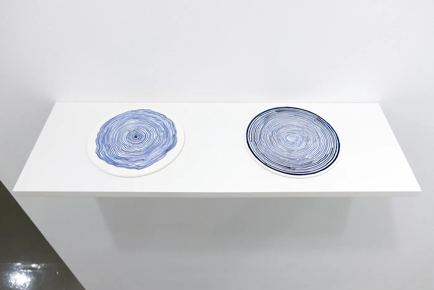 Inside-Out & Outside-In — two ceramic squares with incised concentric circles, side by side on a white wall