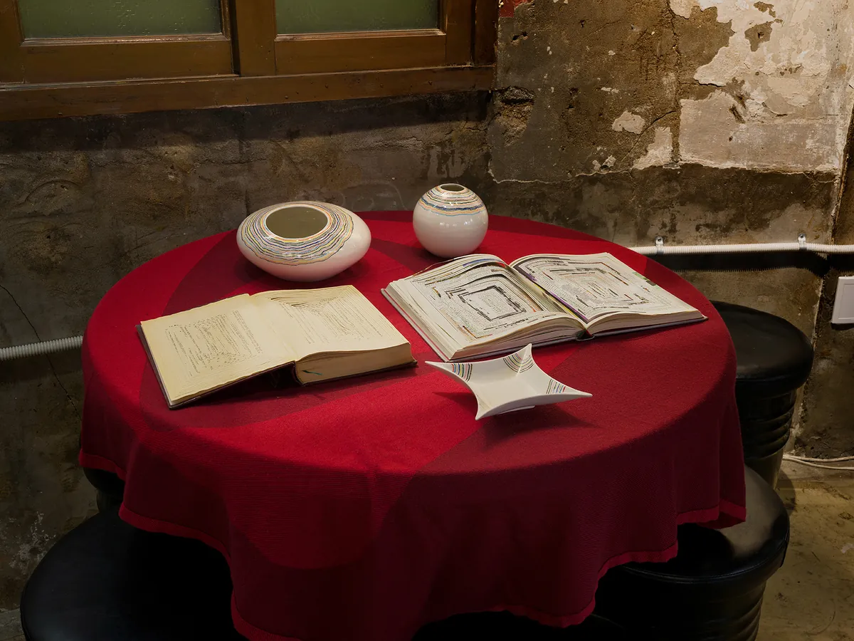 Installation view — ceramic vessels and open sketchbooks on a red table