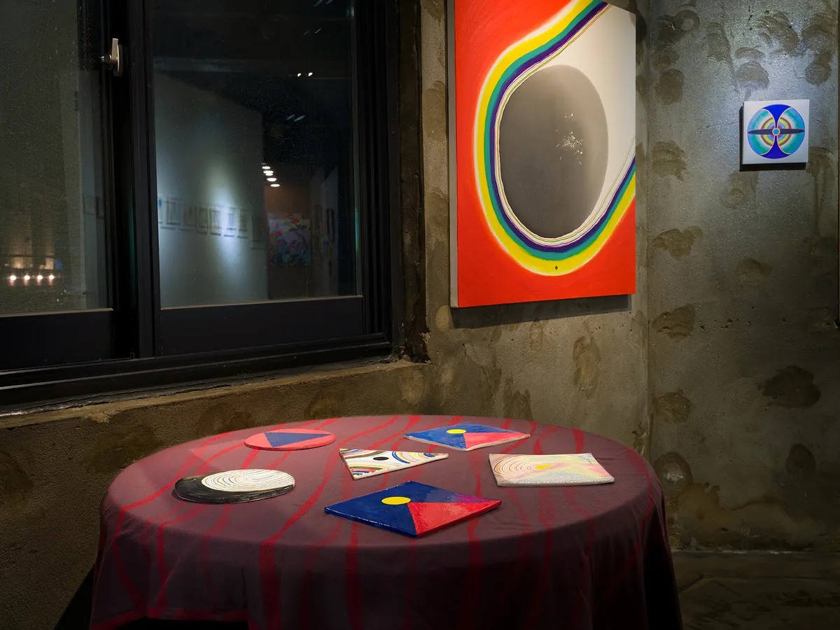 Installation view — red table with shaped works beside a large orange painting