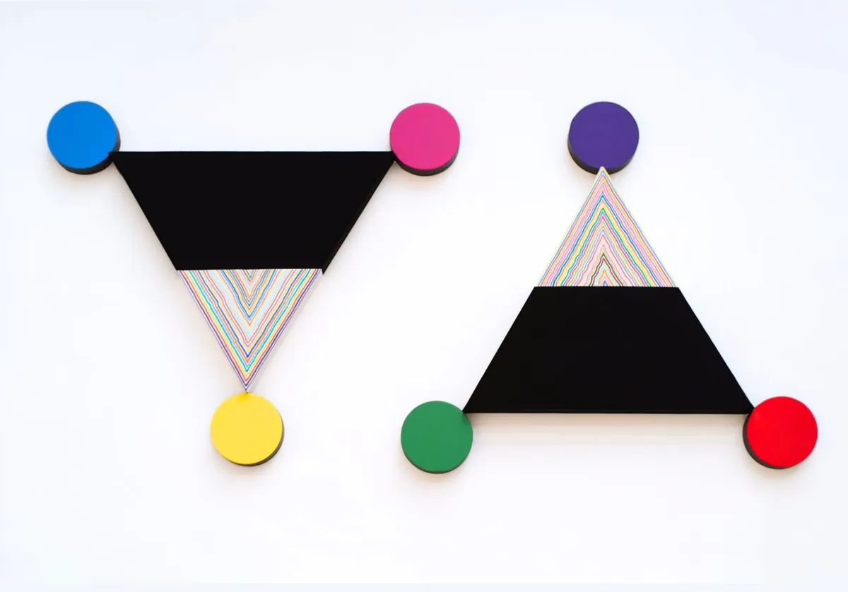 이상의 정의, 2024. Two wall-mounted triangle panels ringed by colored wooden discs at their points, one triangle inverted with a yellow point, one upright with a red point, each half flat black and half filled with rainbow-colored lines